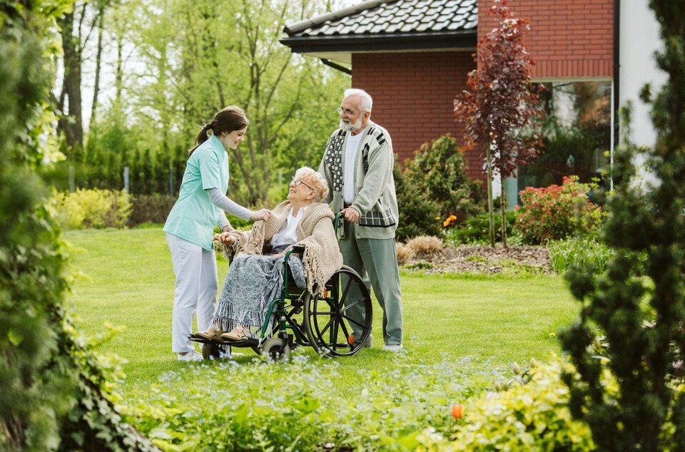Pflegerin mit zwei älteren Leuten im Garten.