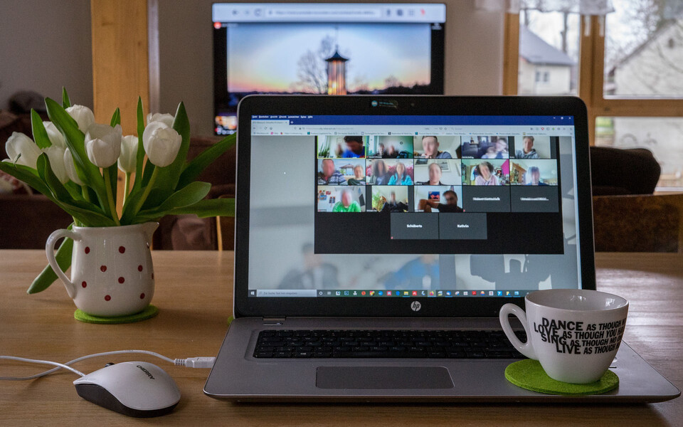offener Laptop it Zoom-Meeting, Kaffeetasse und Tulpen in Vase