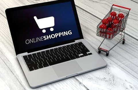 Laptop auf einem Tisch mit kleinem Einkaufswagen symbolisiert den Online-Einkauf